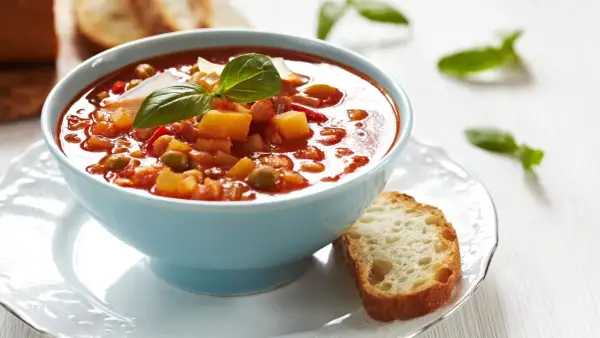 Aksamitna zupa solferino w błękitnej misce, udekorowana bazylią i parmezanem, obok kromka chleba.