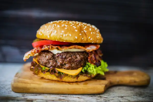 Soczysty burger z wołowiny z bekonem, serem, pomidorem i sałatą na desce.