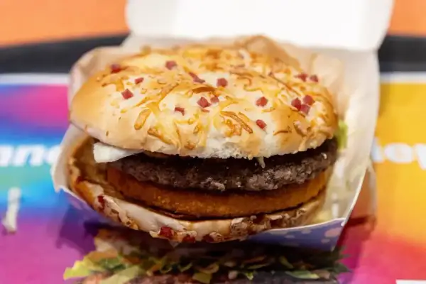 Apetyczny burger drwala z chrupiącą bułką posypaną serem i kawałkami boczku, w środku soczysty kotlet i panierowany dodatek.