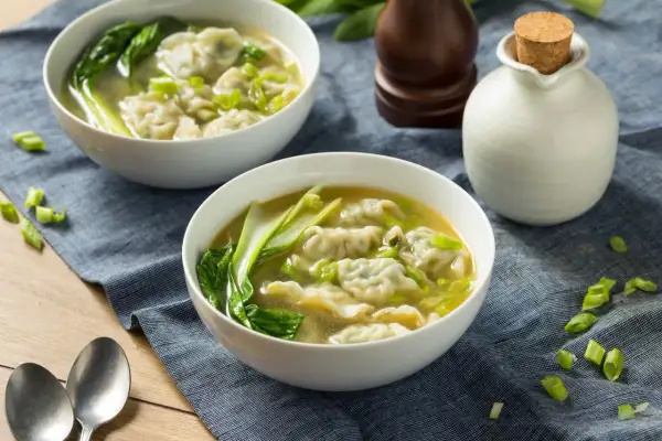 Dwie miseczki aromatycznej zupy won ton z zielonymi warzywami i posiekanym szczypiorkiem.