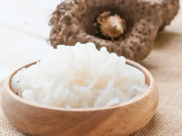 Miseczka pełna białego makaronu z mąki konjac, obok surowa bulwa.