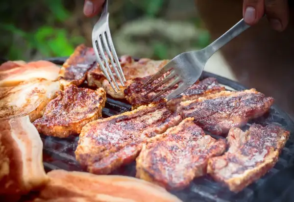 Soczysty boczek na grillu, idealny po marynacie. Dwie widelce sprawdzają stopień wysmażenia.