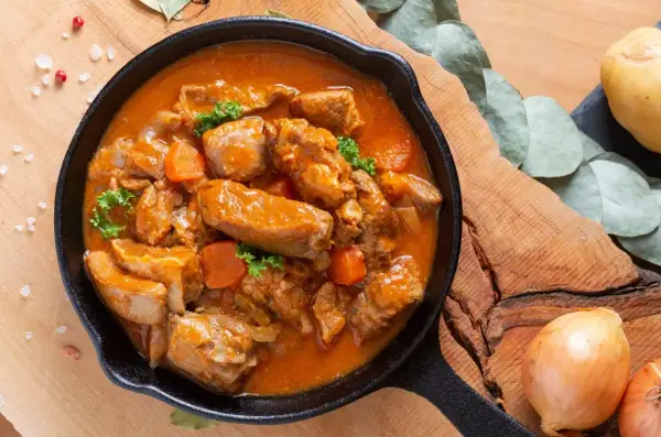 Gulasz z polędwiczki wieprzowej w aromatycznym sosie, z kawałkami marchewki i natki pietruszki, podany w żeliwnej patelni.