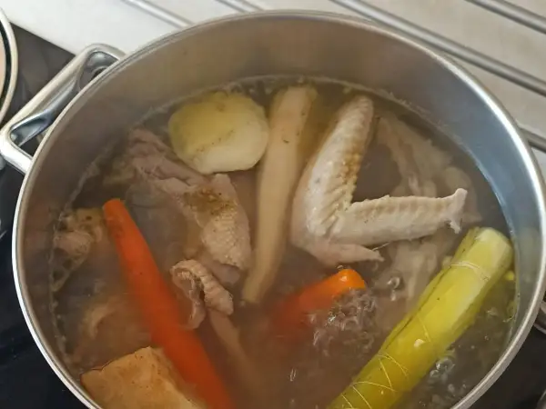 Gotowanie rosołu bez przykrycia. W garnku bulgoczą marchewki, kawałki kurczaka, skrzydełka, por i ziemniaki.