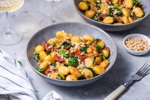 Pyszne gnocchi ze szpinakiem, suszonymi pomidorami i orzeszkami pinii, posypane parmezanem.