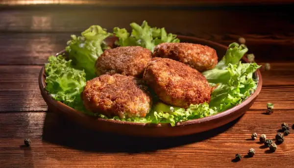 Cztery apetyczne kotlety mielone z airfryer, podane na liściach sałaty, prezentują się wyśmienicie.