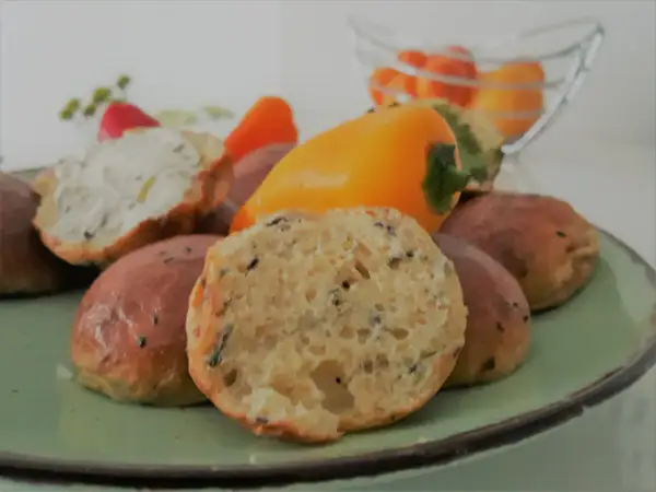 Babka jajowata co to jest? Puszyste bułeczki z ziołami i czarnuszką, jedna przekrojona, obok papryczki i ser.