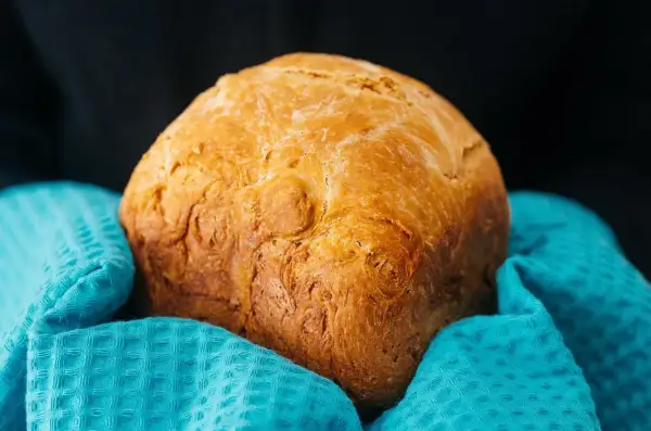 Złocisty chleb z airfryer, pachnący świeżością, otulony turkusowym ręcznikiem. Idealny na śniadanie.
