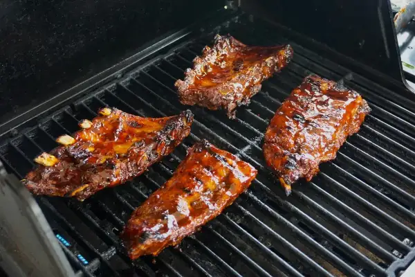 Soczyste żeberka w marynacie do żeberek skwierczą na grillu, nabierając apetycznego koloru.